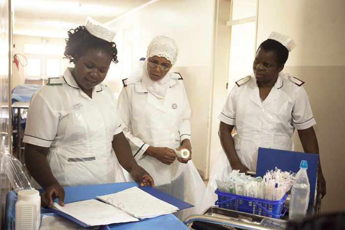 Cameroonian nurses in white uniforms and caps reviewing patient charts in the ward